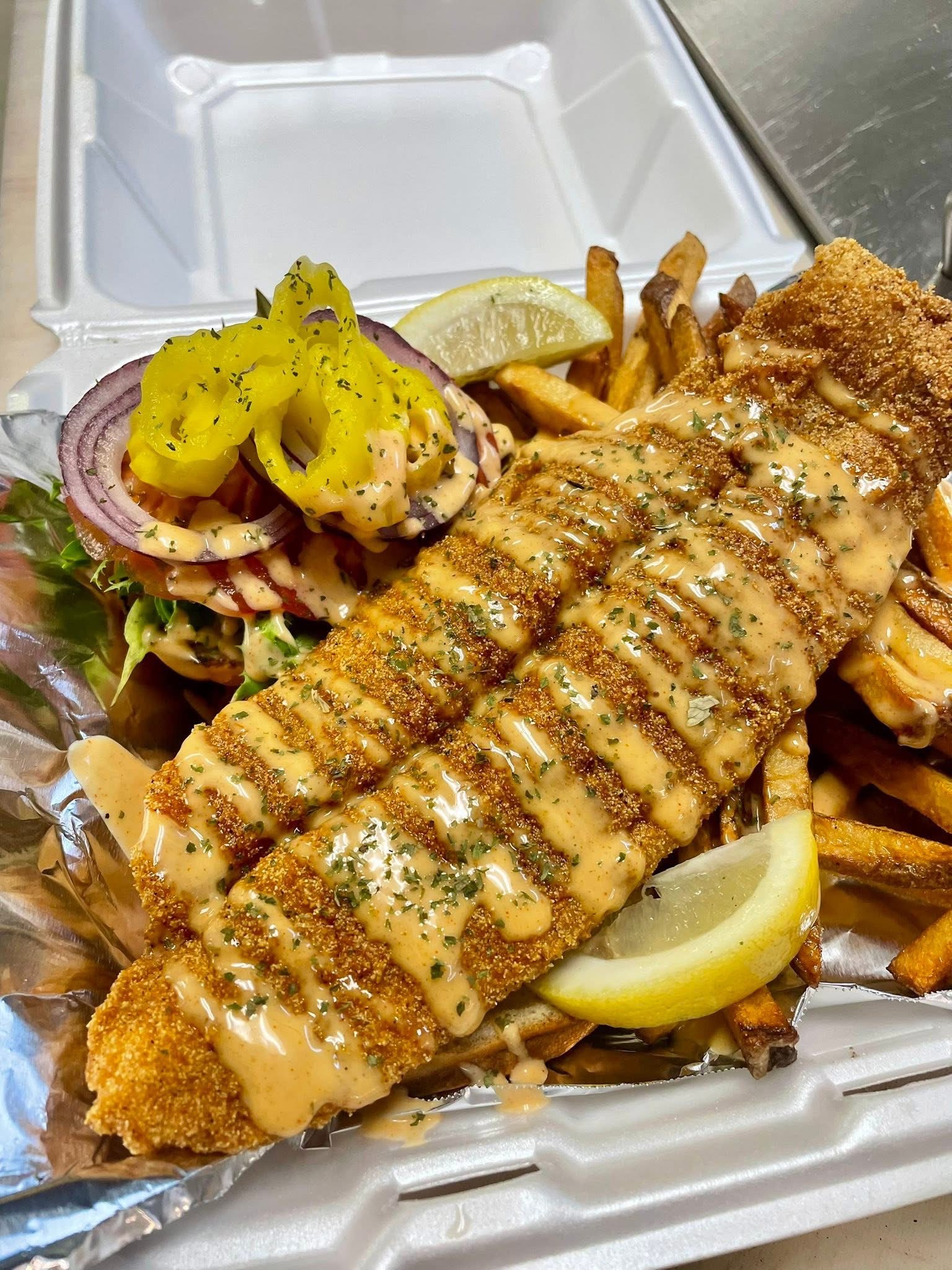 Seasoned fish fillet on a bun with pickles and slaw, fries alongside