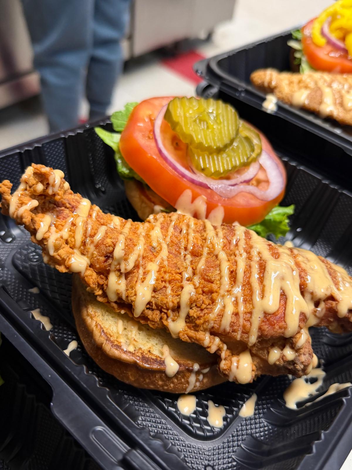 Buttermilk-fried chicken fillet under a house sauce drizzle on a brioche bun, with lettuce, tomato, red onion and pickle