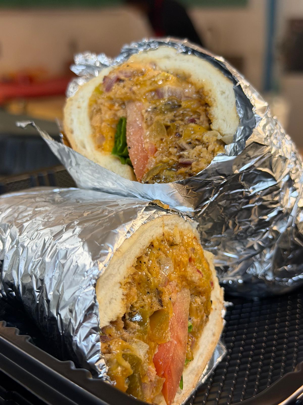 Chop Cheese wrapped in foil and cut in half, chopped beef with melted cheese, peppers, onion and tomato in a hoagie roll