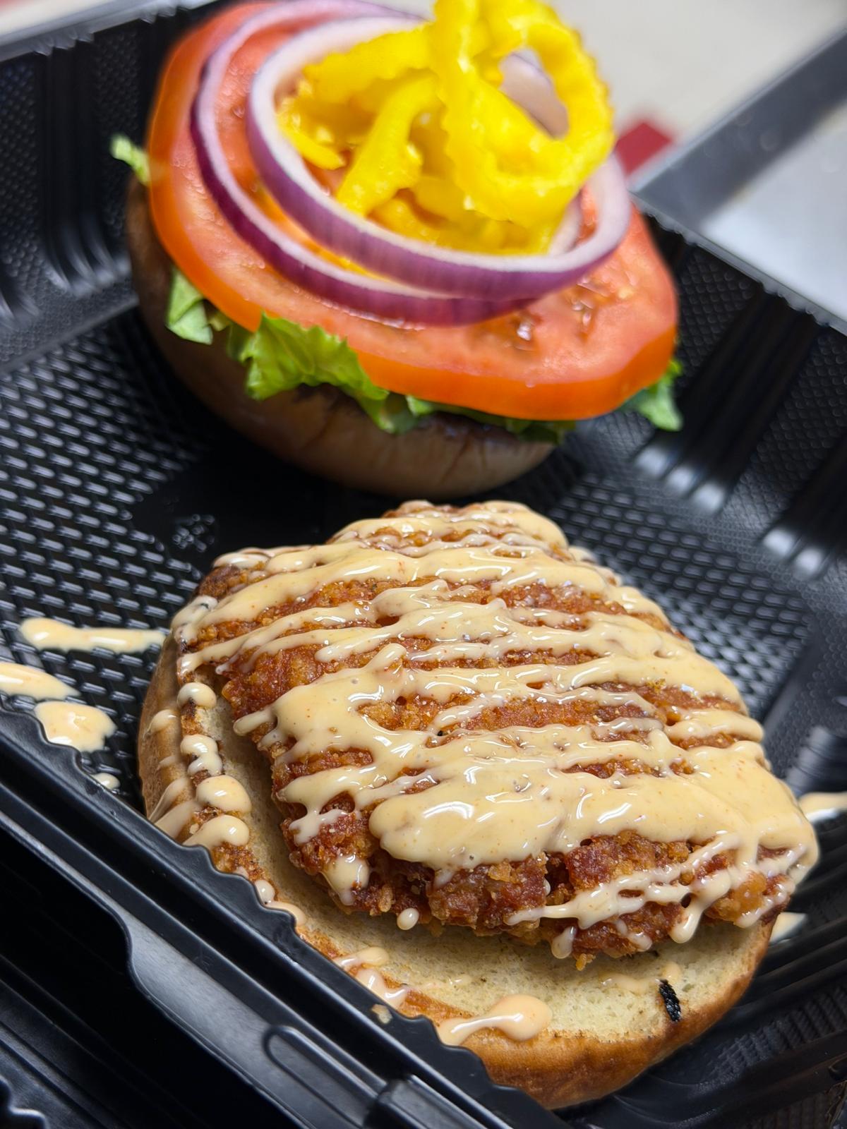 The FishBurger open in its tray — a breaded fillet under a house sauce drizzle, with lettuce, tomato, red onion and banana peppers on the top bun